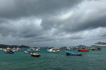 A peaceful coastal harbor filled with small wooden fishing boats gently floating on clear, shallow turquoise water. 