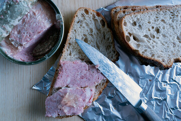A close up of slice of bread with a knife on it next to a can of spam. Scene is casual and relaxed, as it is a simple meal being prepared