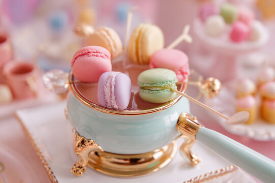 Colorful macarons displayed in a fancy pot at a dessert table during a festive gathering