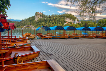 Traditional wooden pletna boats docked along the calm waters of Lake Bled, Slovenia, surrounded by...