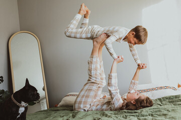 Sister playing airplane with her younger brother on the bed, fun and joyful family moment in cozy matching pajamas at home.
