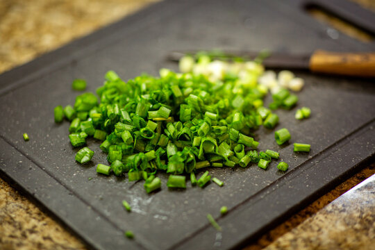 Close-up of a pile of freshly chopped green spring onions on a dark cutting board, with a knife and granite background