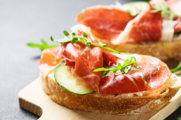 Open sandwiches with prosciutto and arugula on cutting board at white background. Close up image.
