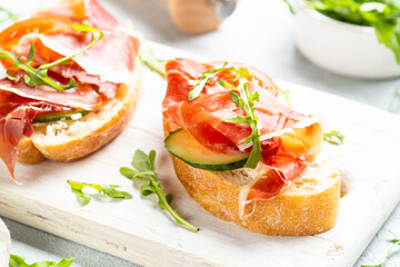 Open sandwiches with prosciutto and arugula on cutting board at white background. Close up image.
