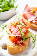 Open sandwiches with prosciutto and arugula on cutting board at white background. Close up image.