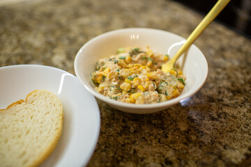 Close-up of a golden spoon lifting a mixture of tuna, corn, and eggs from a glass bowl while preparing a healthy homemade salad
