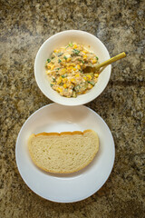 Close-up of a golden spoon lifting a mixture of tuna, corn, and eggs from a glass bowl while preparing a healthy homemade salad