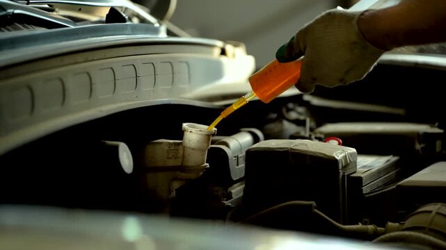A car mechanic extracts used brake fluid using a syringe at a service center.