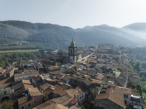 Aerial view of warm terracotta rooftops nestled around the towering church steeple, contrasting against the hazy blue mountains in the distance, Sant Agata de Goti, Campania, Italy.