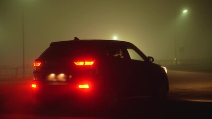 A lonely car stands in the fog at night with its headlights on