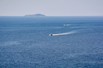 Two speedboats leave white wakes on the vast Adriatic sea. A distant island on the horizon under a summer sky. Concept of speed, freedom, and vacation.