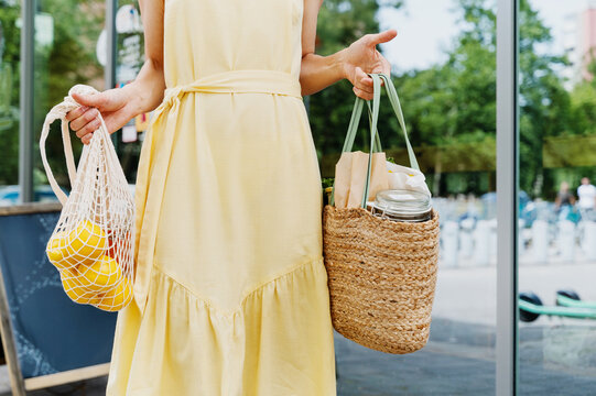 Woman holding bags with fresh organic food on storefront background of zero waste shop.