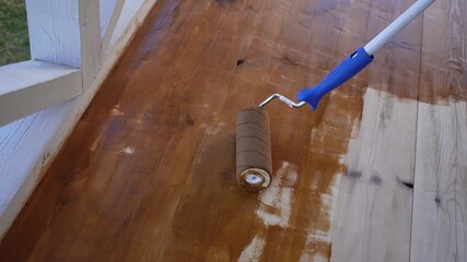Smooth wooden deck stain transformation with paint roller in progress
