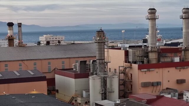 Industrial landscape featuring large chimneys of the Virgen de &Aacute;frica Electrical Substation in Ceuta, Spanish town in North Africa. A modern energy facility set against a Mediterranean urban backdrop.