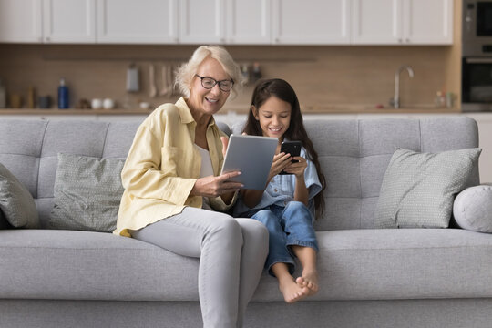 Granny holding tablet sharing information with preteen granddaughter using phone
