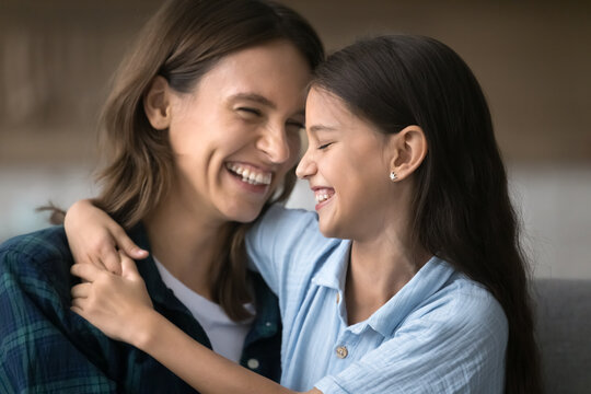Laughing tween girl adopted child embracing affectionate millennial foster mom