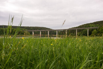 A massive bridge stretches across a river with forested hills and mountains in the background. Scenic natural landscape, calm water, and tranquil outdoor environment.