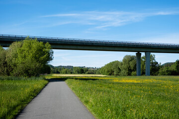 A scenic cycling path runs along natural dirt terrain surrounded by forest and open meadows....
