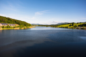 A stunning lake landscape framed by forest trees and distant mountains. Calm water, natural colors, and peaceful scenery create a perfect outdoor nature view.