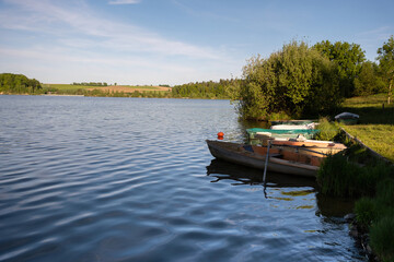 Small rental and fishing boats float near the lake shore, surrounded by lush greenery. Calm water and natural scenery create a peaceful outdoor setting for recreation and nature.