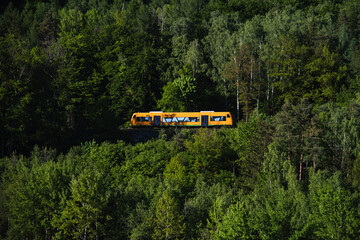 A yellow intercity electric train moves through distant mountains and dense forest. Scenic outdoor setting capturing transportation, travel, and natural landscapes.