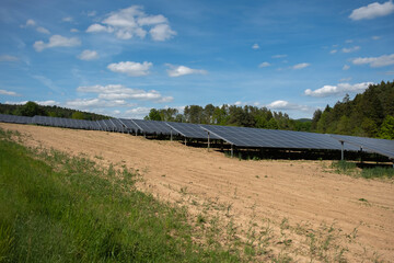 Rows of solar panels cover a field with mountains and forest in the background. Clean energy concept in a natural landscape with sunlight and sustainable technology.