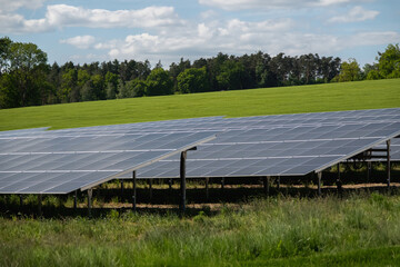 Rows of solar panels cover a field with mountains and forest in the background. Clean energy concept in a natural landscape with sunlight and sustainable technology.