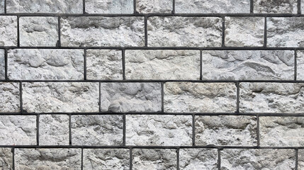 Close-up of a gray stone wall made of rectangular blocks with rough, uneven surfaces and visible mortar lines, creating a textured architectural pattern.