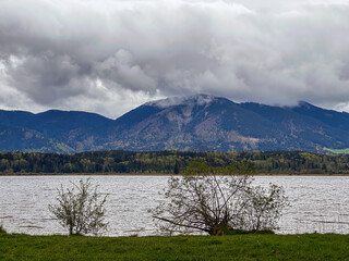 A stunning lake landscape framed by forest trees and distant mountains. Calm water, natural colors, and peaceful scenery create a perfect outdoor nature view.