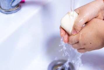 Fototapeta premium A child's hands are being washed with soap under a running tap.