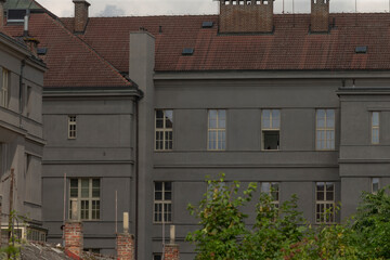 grey residential building side with repeating windows and muted roofline, leafy foreground and calm
