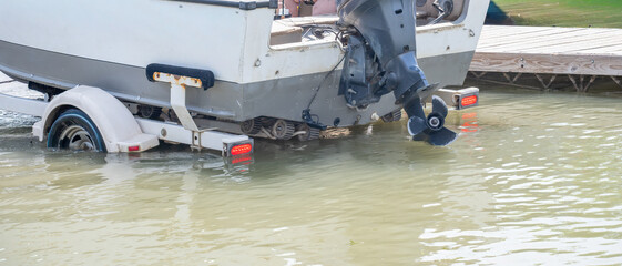 Selective focus on a boat as a trailer is backed down a ramp to load.