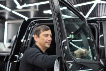 Obraz premium Male car service worker glue window tinting in luxury car detailing car repair the concept of love for cars and protection. Applying tinting foil on a car window in the tuning studio close-up. 
