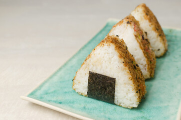 Onigiri, traditional Japanese food, two pieces in crispy breading on a turquoise ceramic plate. Boiled rice with filling in the middle with nori. Fast food concept. Selective focus. Copy space