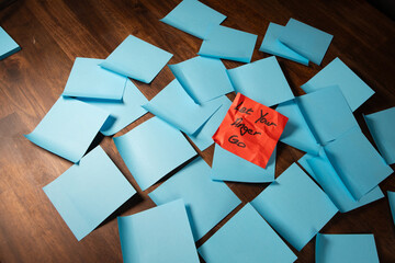 Red crumpled sticky note on a pile of blue sticky notes placed on a dark wood surface with text reading let your anger go.