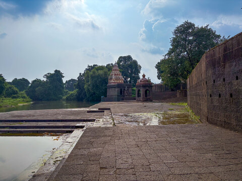 A peaceful riverside view of an ancient temple complex in Wai, Maharashtra, featuring stone ghats, lush greenery, and traditional temple architecture under a soft, cloudy sky.