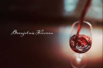 Obraz premium Verre de vin rouge en cours de remplissage avec texte en français « Beaujolais Nouveau », célébration traditionnelle du 3ᵉ jeudi de novembre liée à la sortie du vin primeur