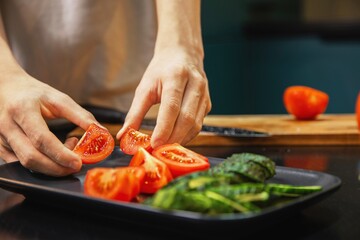 Person arranging sliced tomatoes and cucumbers on a plate while preparing a fresh salad in the kitchen. Healthy eating, fresh vegetables, and clean food preparation at home.
