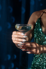 woman holding a glass of champagne, woman  in festive shiny clothes with a glass of champagne, hands on a blue fabric background, blue velvet curtains, Holiday party, corporate event, new year celebra
