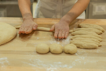 Hands of baker rolling dough on wooden surface flour shaped pieces preparation