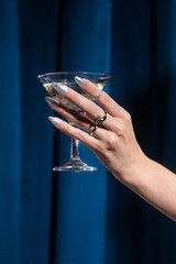 hands of a woman with a glass of champagne, hands on a blue fabric background, blue velvet curtains, martini glass, Holiday party, corporate event, new year celebration