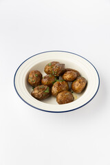 Roasted baby potatoes with fresh herbs in a white bowl on a clean studio background
