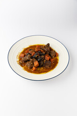 Beef stew with carrots and prunes in rich gravy, served on plate, isolated on white