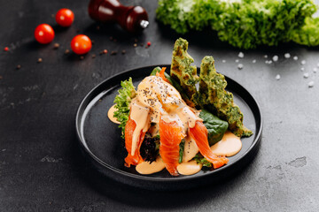 Smoked salmon salad with poached egg, hollandaise and spinach waffles on black plate