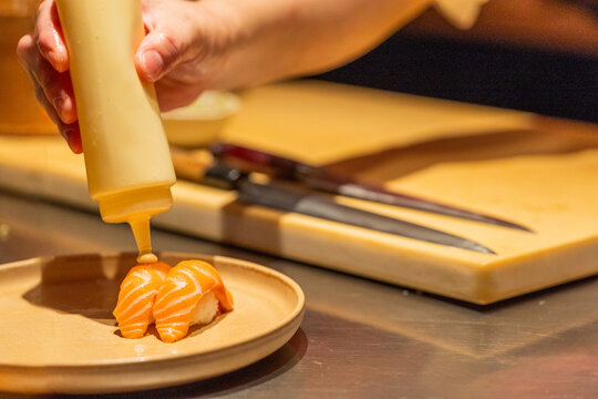 Hand drizzling sauce over sushi on plate in modern kitchen setting