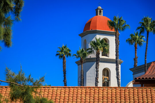 Mission San Juan Capistrano orange dome rises above tile roofs and palm trees