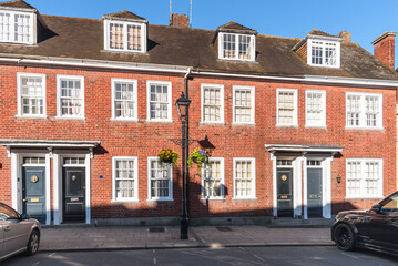 Traditional British brick terraced houses along a stone pavement on a sunny spring day. Parking spaces are in front of the houses.
