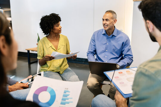 Business coach guiding team while reviewing project charts. Coworkers learning during training session. Leadership and productivity concept. - Powered by Adobe