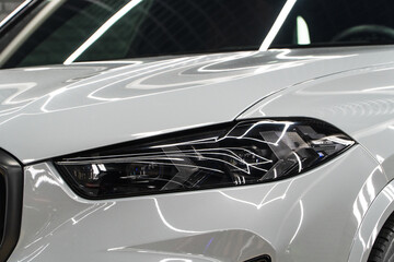 Fototapeta premium Close up detail on one of the LED Laser headlights modern white car. Exterior close up detail. Headlights of car. BI-LED Laser headlights of a modern white car. Front BI-LED headlight on sport car.