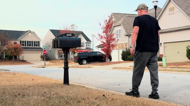 man walks to mailbox and checks for mail in suburban neighborhood